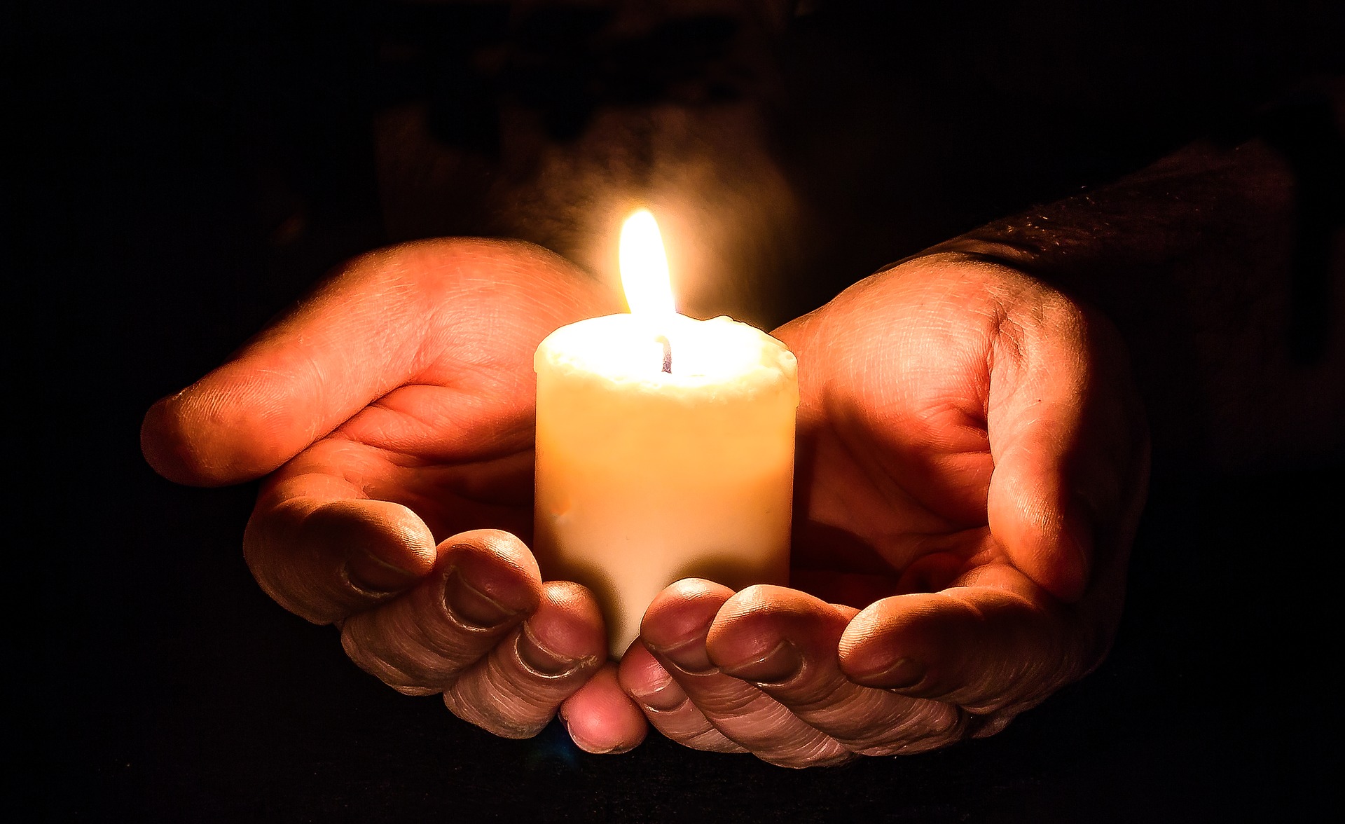 Hands holding a lit candle.