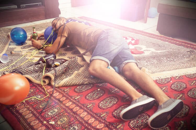 Party, drunk and hangover with a man sleeping on a living room floor after new year celebration. Beer, college and hungover with a male passed out after a frat house birthday event for spring break blackout drunk
