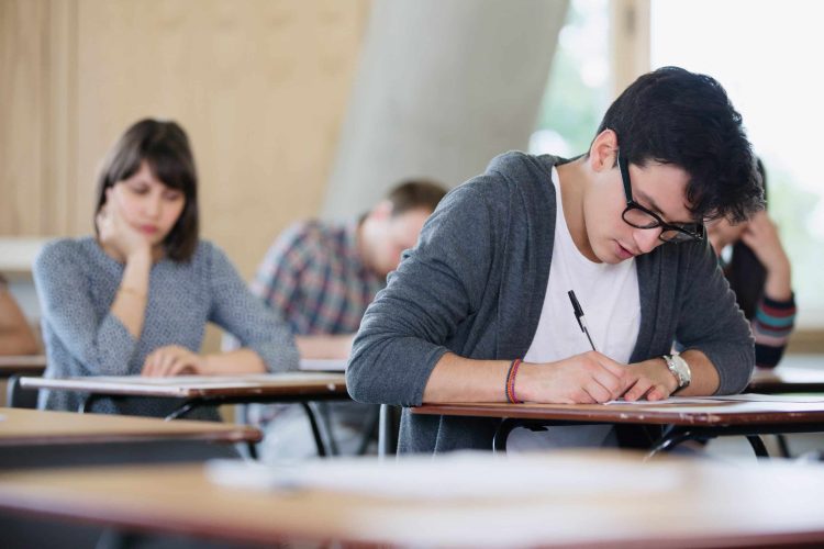Focused male college student taking test at desk in classroom grades